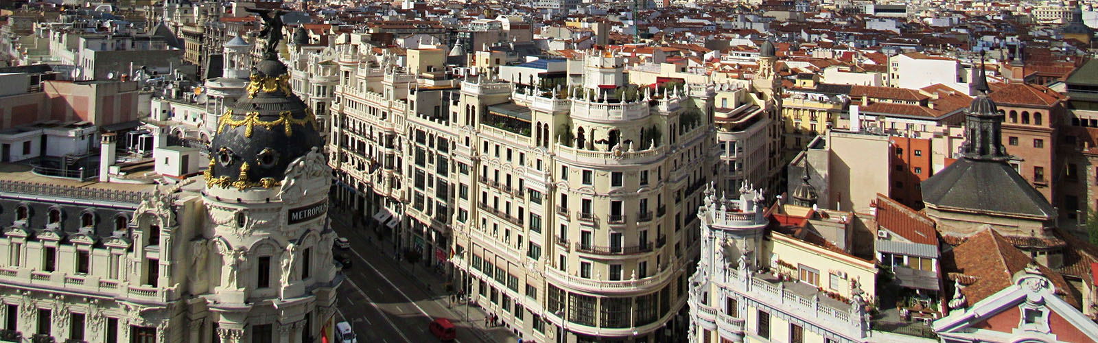Old and densely-packed white buildings lining a wide street. Red-roofed buildings stretch to the horizon.